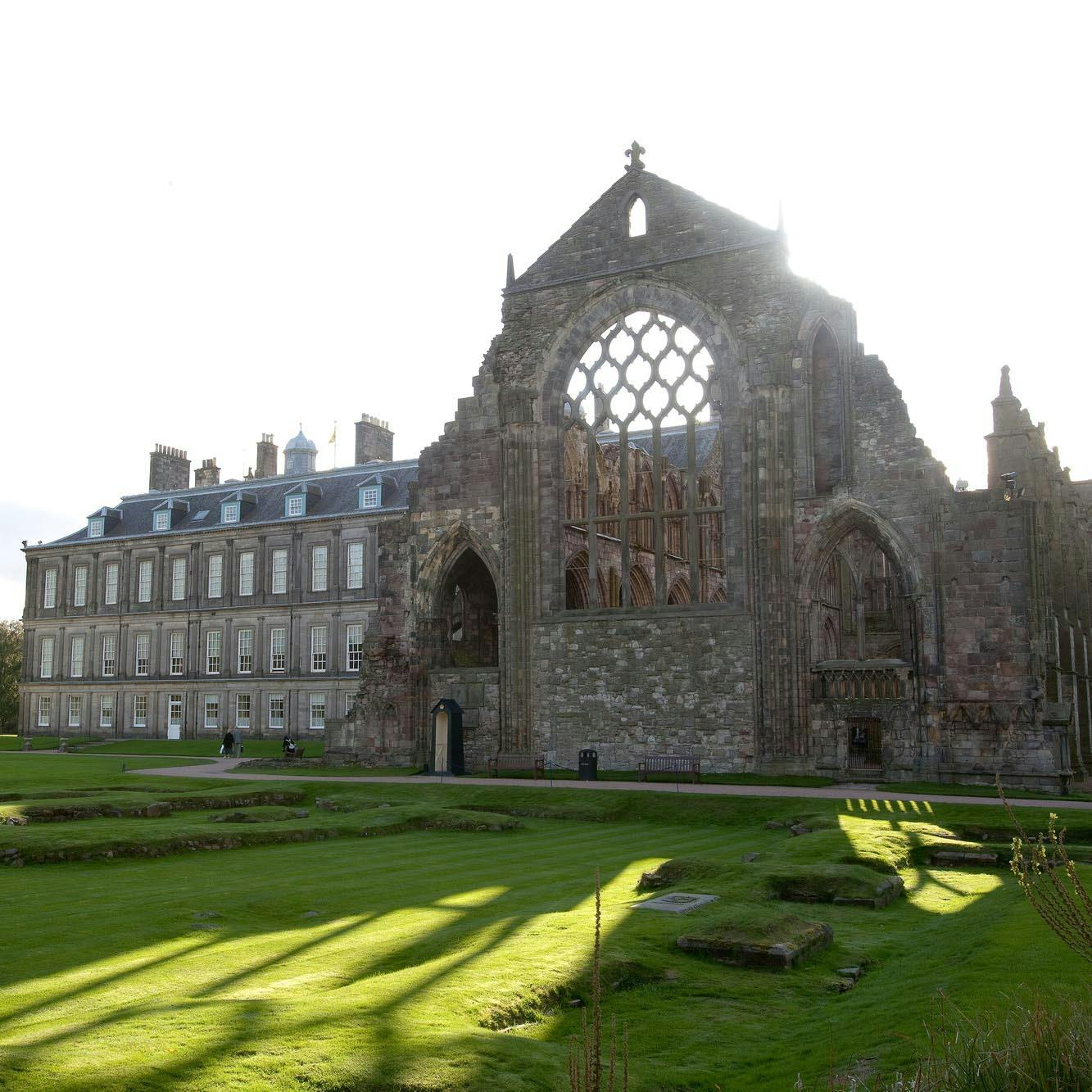 一座历史悠久的大型石头遗址，拱形的窗户矗立在一座长长的多层建筑旁，周围环绕着一片保养良好的草坪。