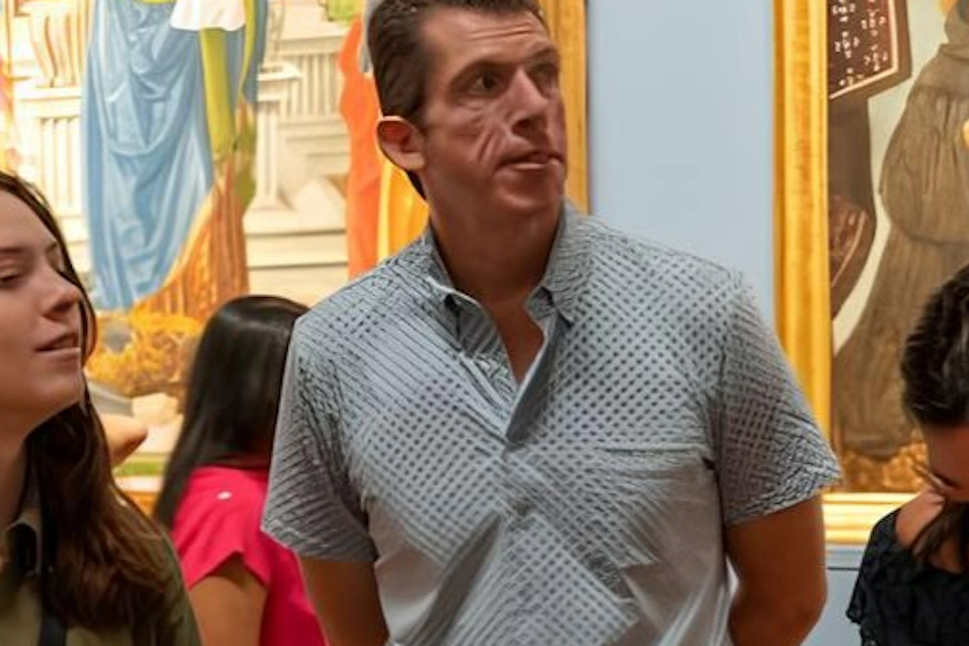 A group of people stand and interact inside an art gallery, with large, framed paintings visible on the walls in the background.