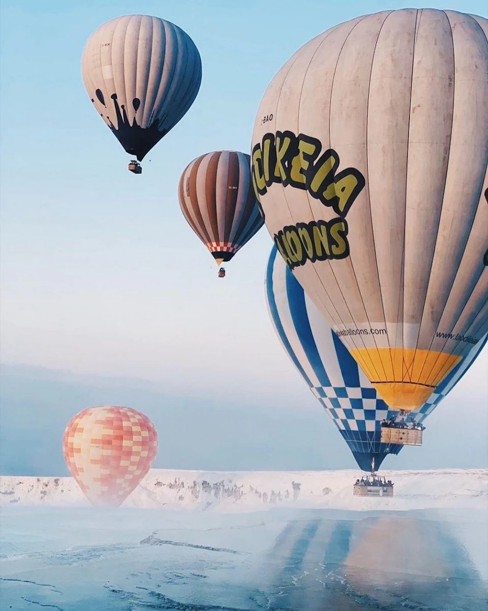 Hot air balloons of various colors and patterns floating in a blue sky above a snowy landscape.