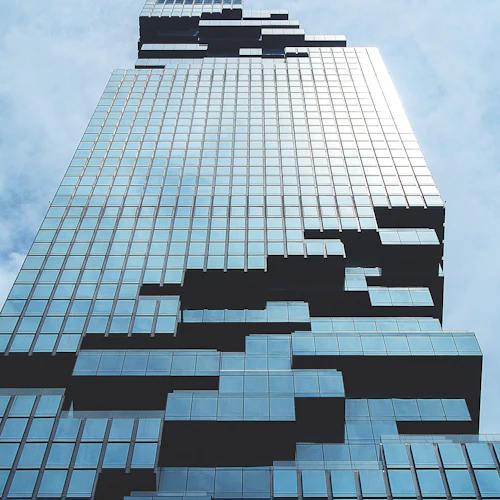 Ein moderner Wolkenkratzer mit einer gläsernen Fassade und gestaffelten Balkonen vor einem wolkenverhangenen Himmel.