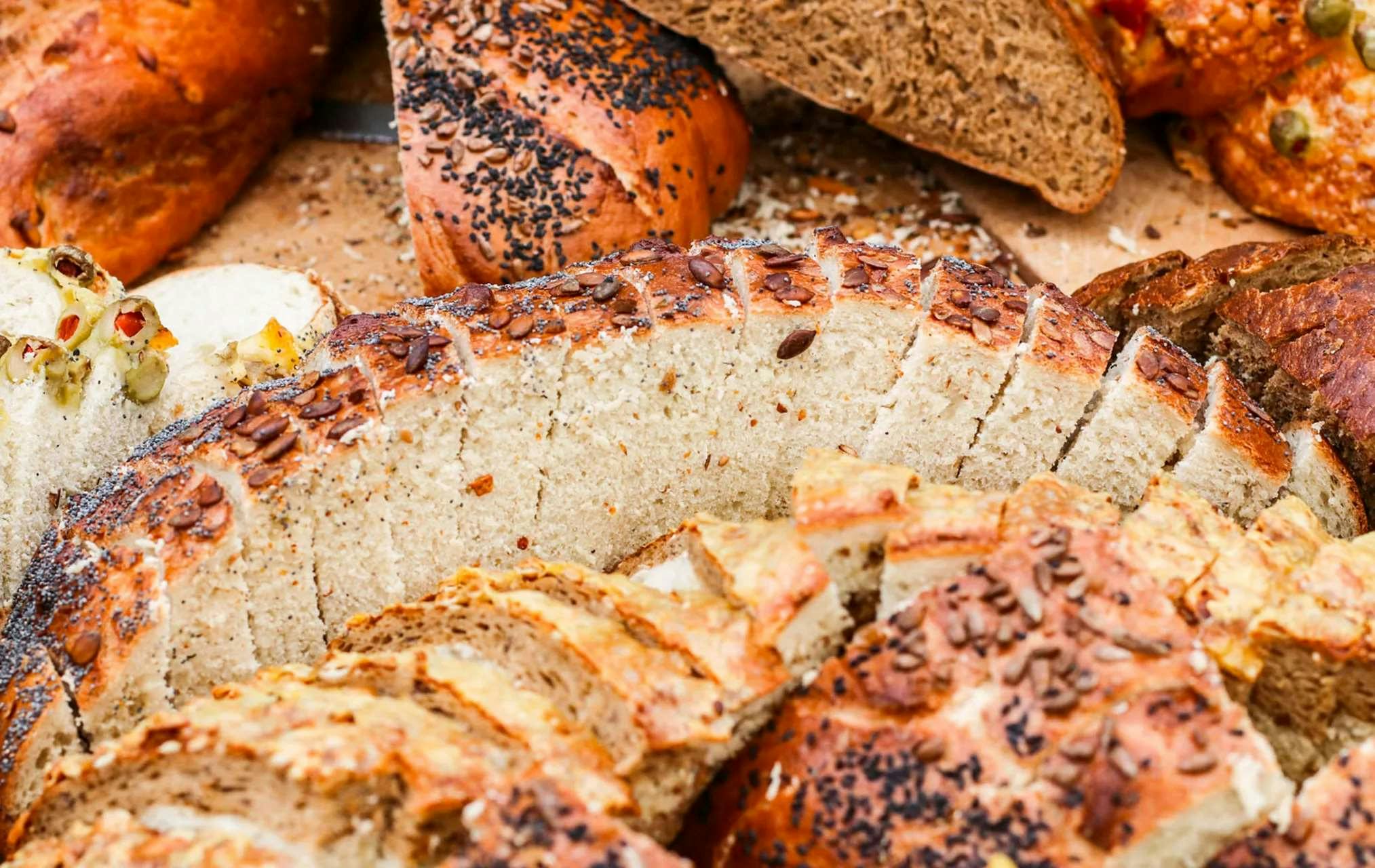 Close-up of various types of sliced bread, including loaves topped with seeds and a mix of white and whole grain bread.