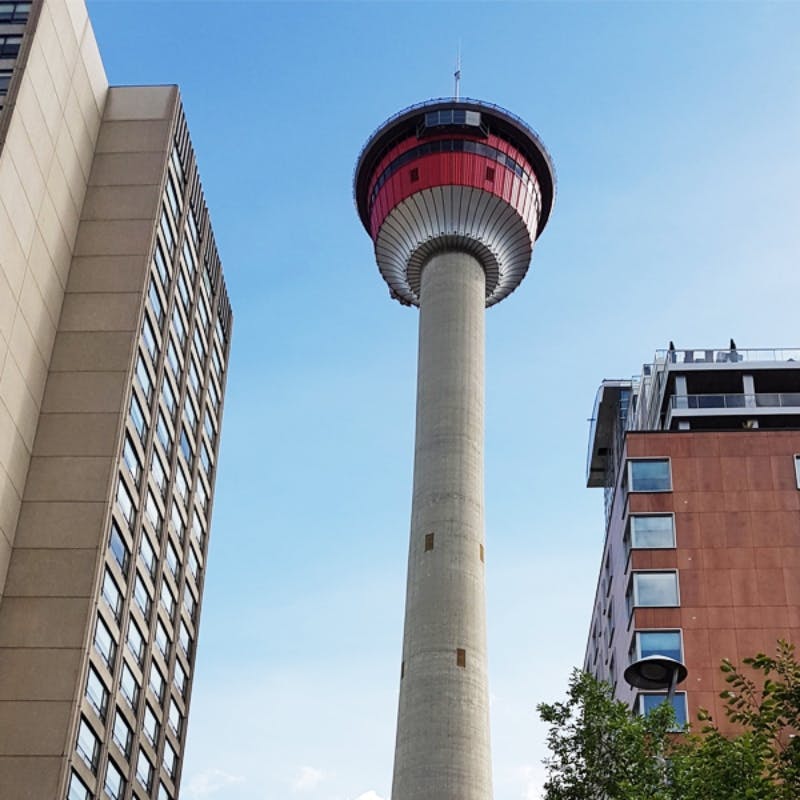 Beton observationstårn med et rødt observationsdæk mellem to høje bygninger under en klar blå himmel.