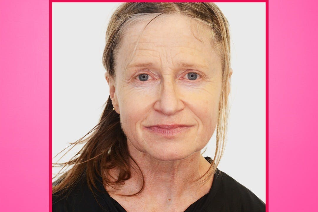 Μια γυναίκα με ανοιχτόχρωμα μαλλιά δεμένα πίσω, φορώντας μια μαύρη μπλούζα, κοιτάζει απευθείας την κάμερα σε ένα απλό λευκό φόντο με ροζ περίγραμμα.