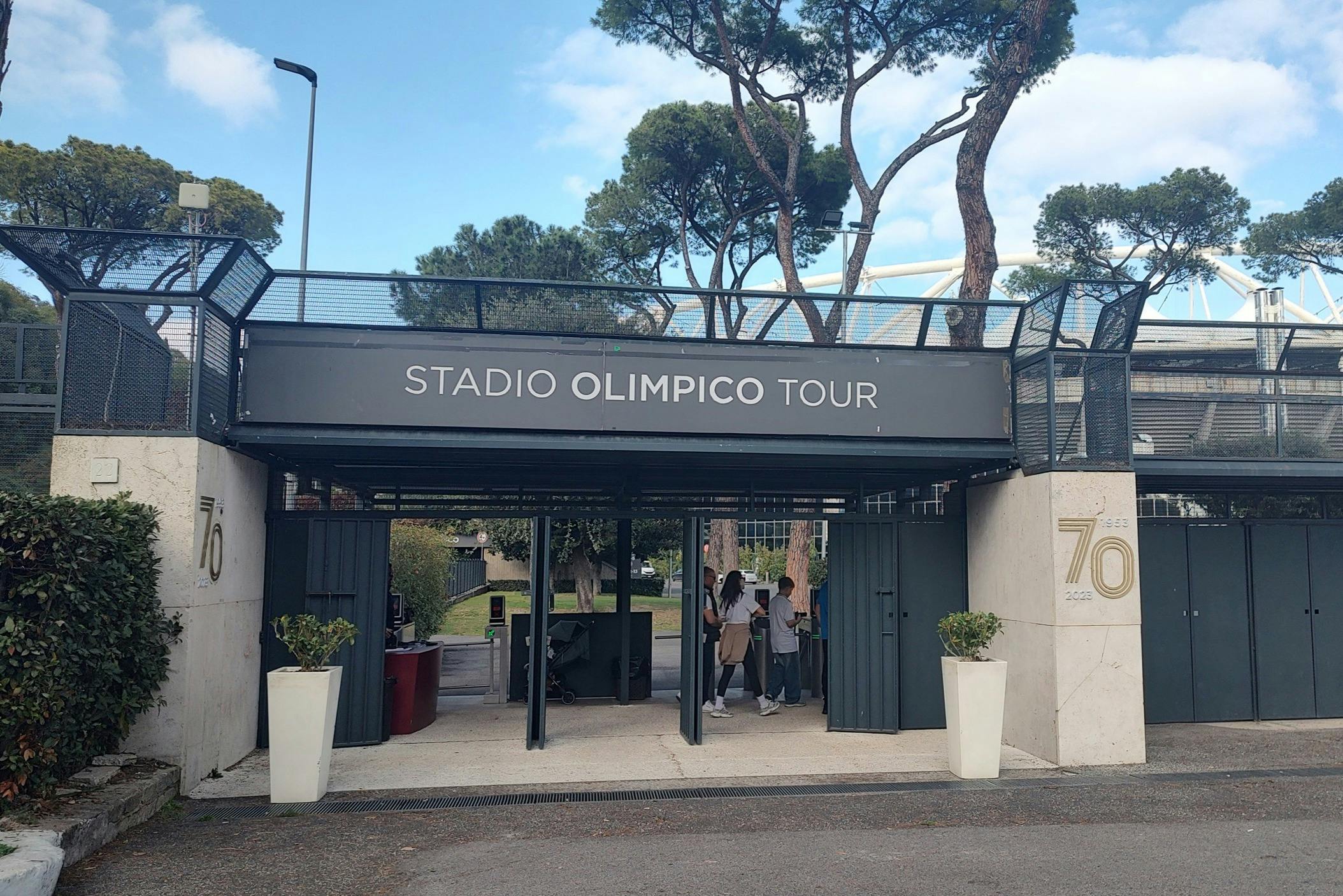Toegang tot het Stadio Olimpico Tour met mensen die doorlopen, omringd door bomen en een heldere hemel.