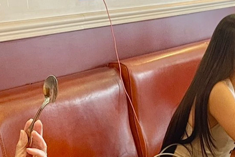 A woman smiling and holding a spoon at a restaurant table with food, drinks, and others seated in the background.