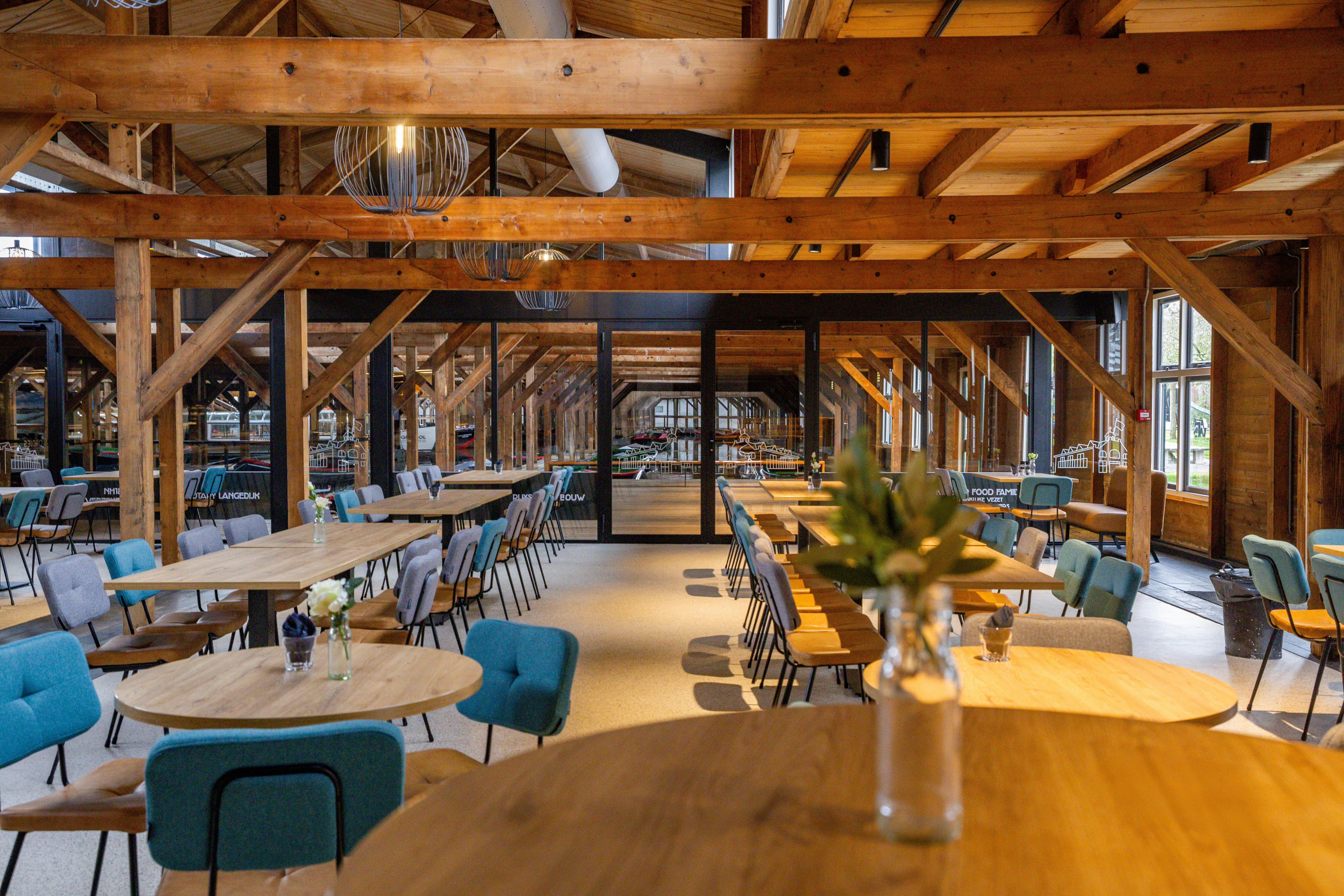 Een ruim restaurantinterieur met houten balken, moderne meubels en gedekte tafels met bloemen in vazen.