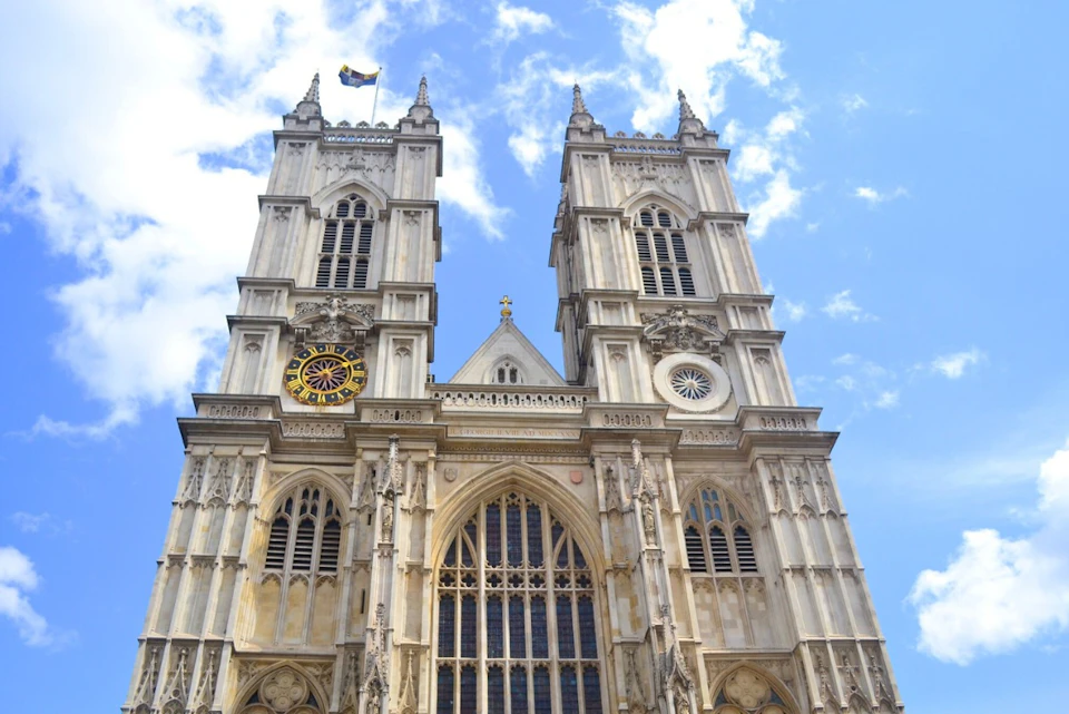 The facade of a large Gothic-style cathedral with tall twin towers and detailed architecture under a blue sky.