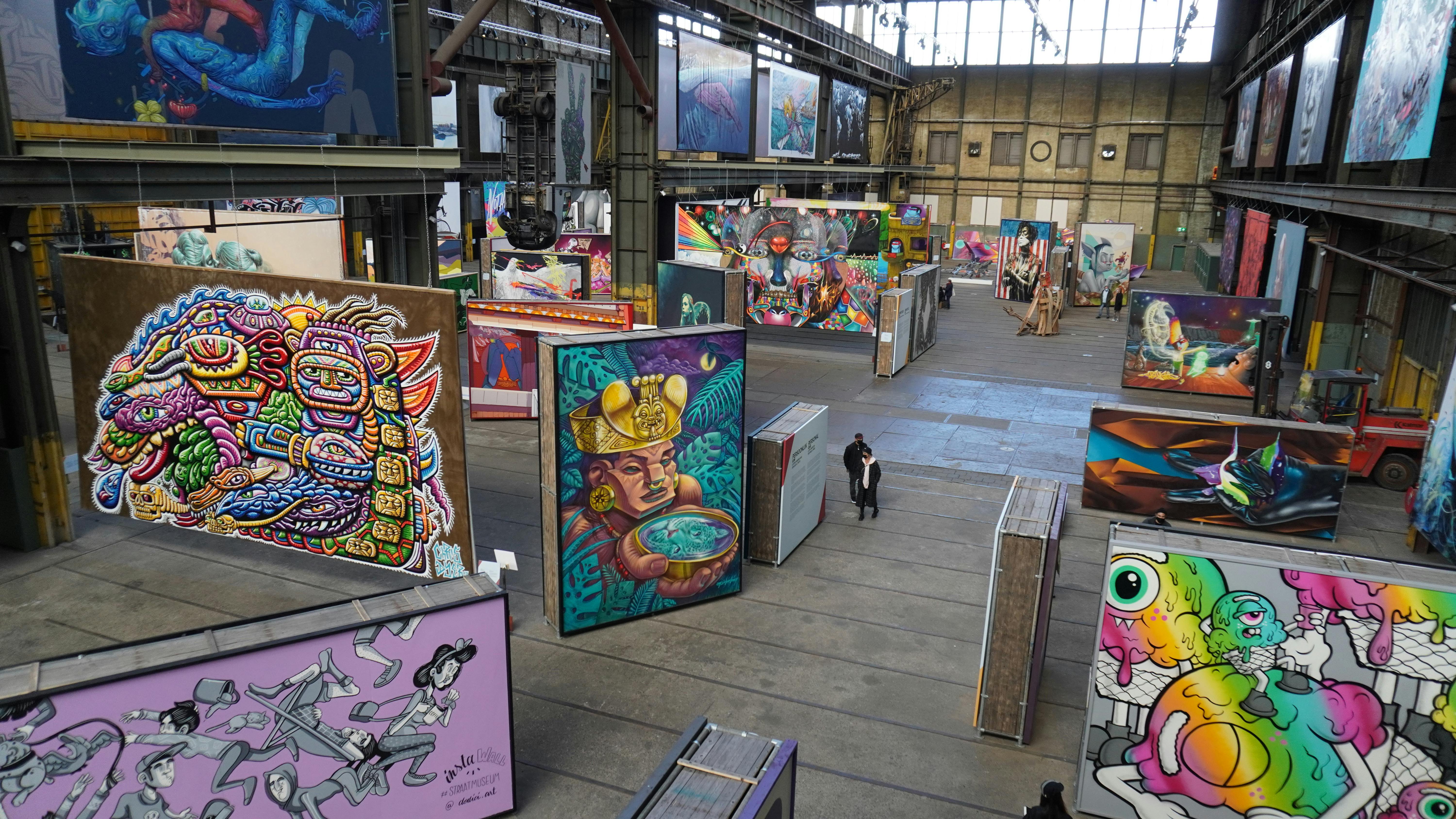 산업 공간에 활기차고 다채로운 벽화와 그림이 전시된 대형 실내 전시회. 브라우징하는 사람은 거의 없습니다.