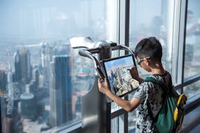 Giovane uomo che guarda la vista su uno schermo digitale al 124° piano del Burj Khalifa.