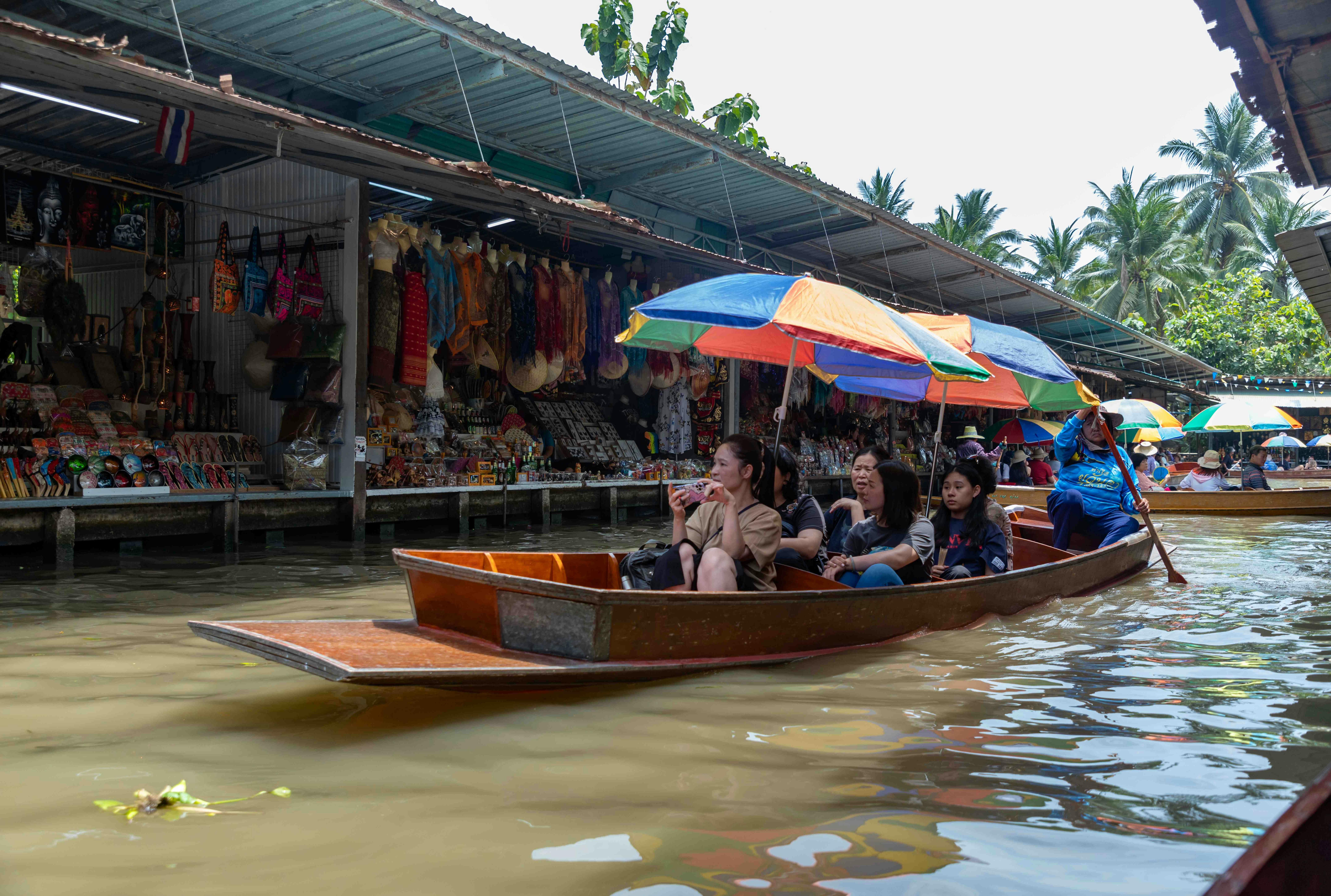 People riding colorful boats in a floating market with goods displayed along the water under canopies.