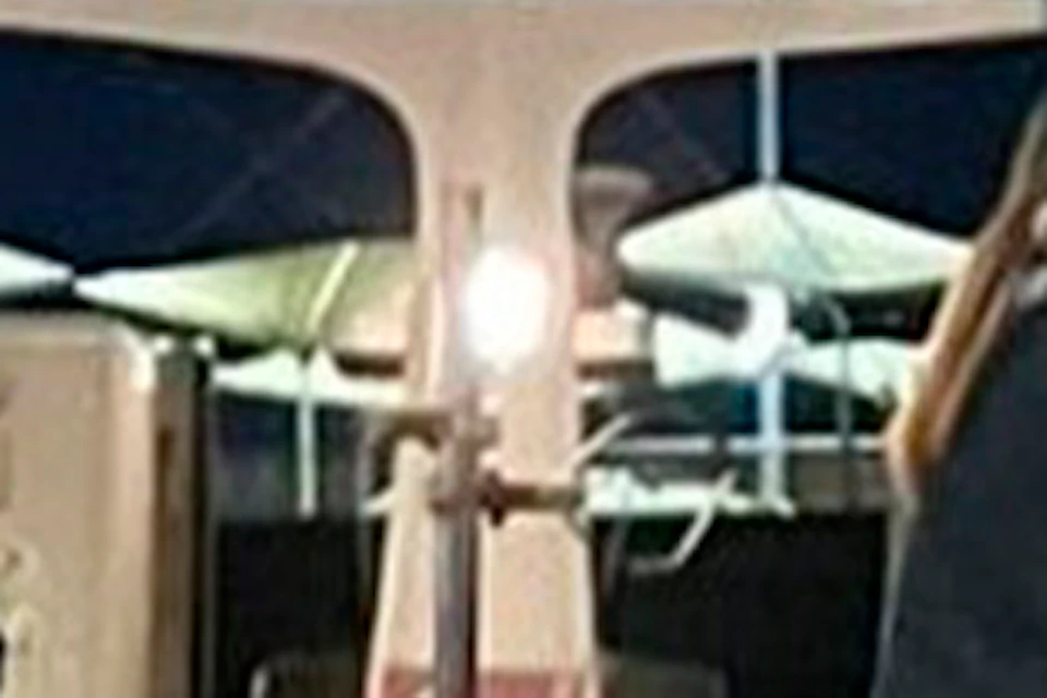 People sitting around tables on a boat at night, engaged in a wine tasting event, with two servers in the middle.