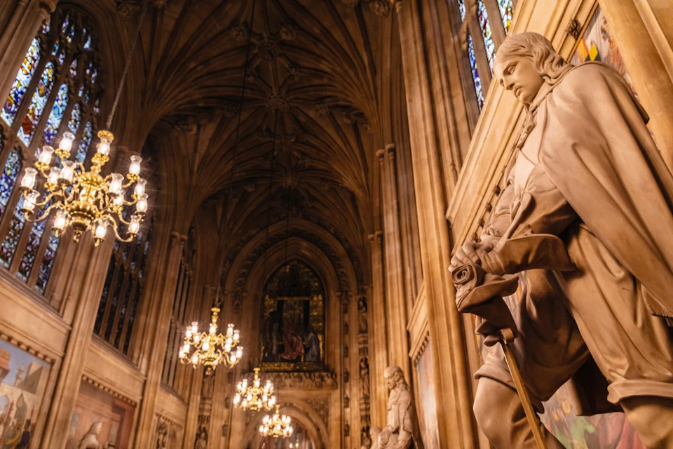 Ornate cathedral interior with arched ceiling, chandeliers, large statues, and stained glass windows on the right side.