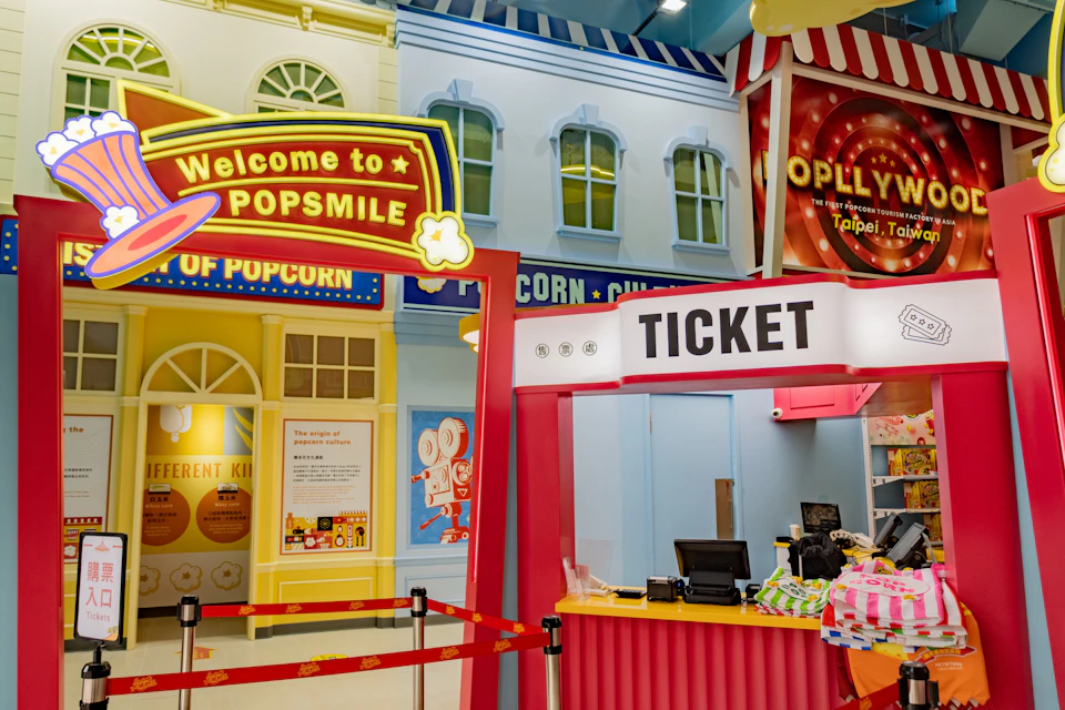 A colorful ticket booth in an amusement or themed area with signs and decorations, including popcorn imagery.