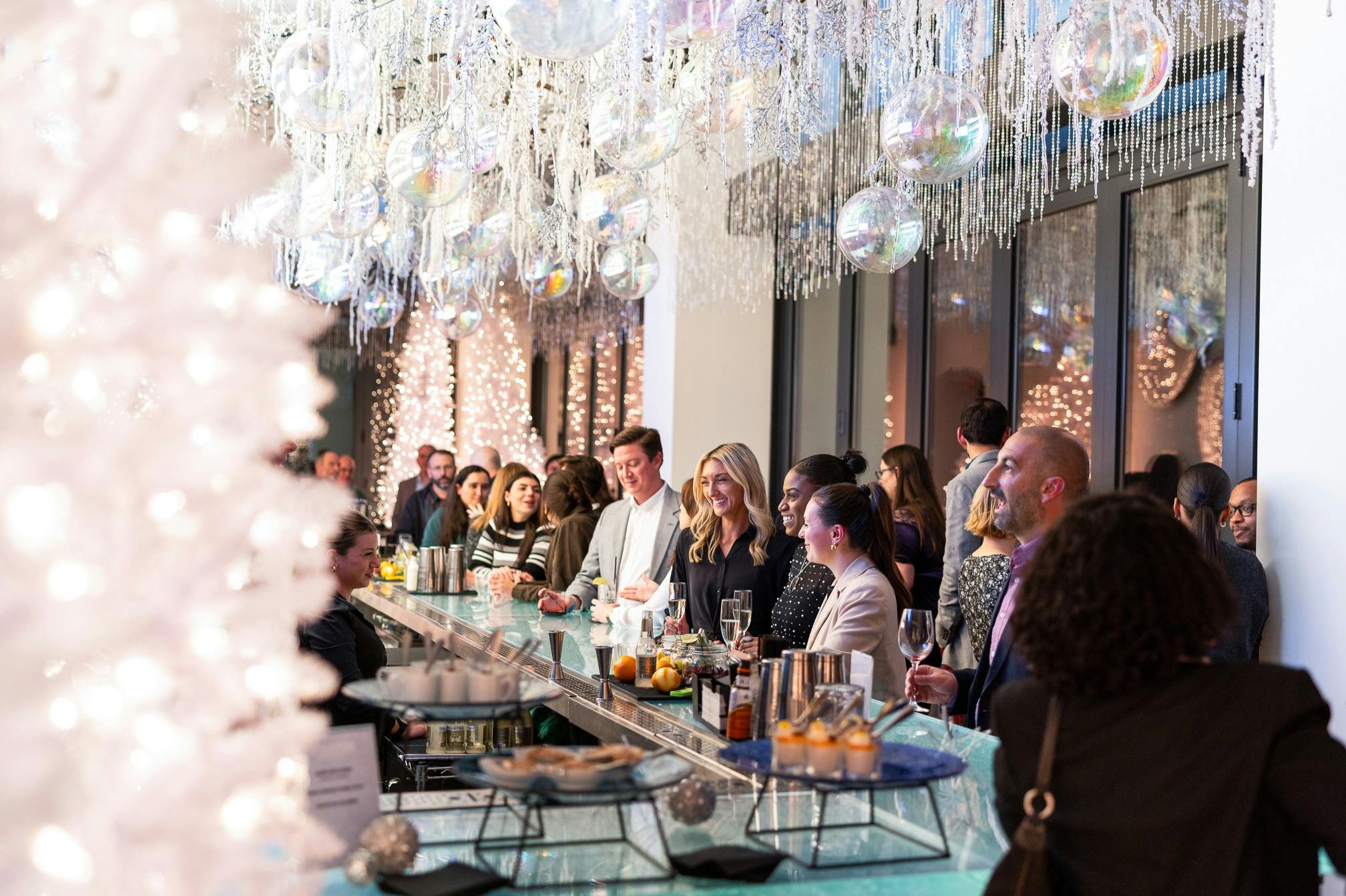 People gather at a brightly lit bar with hanging decorations and disco balls, enjoying drinks and socializing.