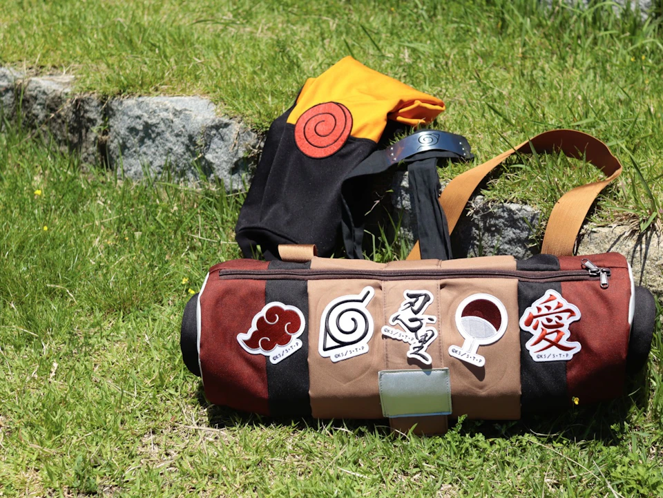 A backpack and a cylindrical bag featuring symbols and designs, placed on grass near rocks in an outdoor setting.
