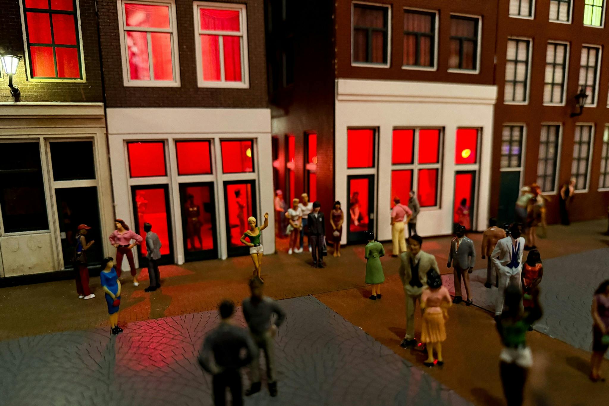 Miniatyr gatubild med små figurer framför byggnader med rödbelysta fönster, som visar en urban miljö.