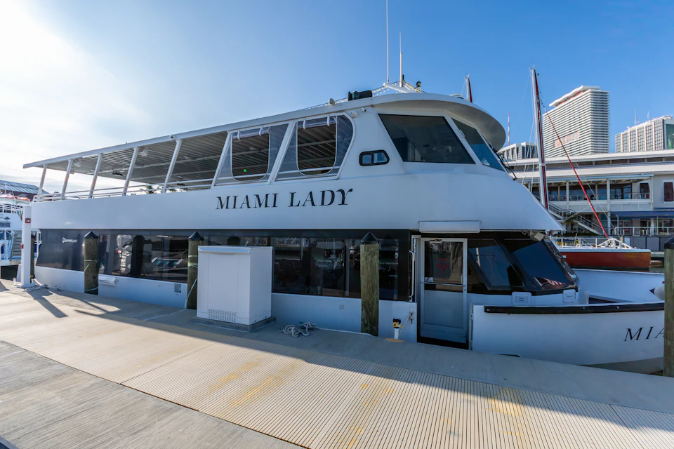 A docked boat named "Miami Lady" with a white and blue exterior, moored at a marina on a clear, sunny day.