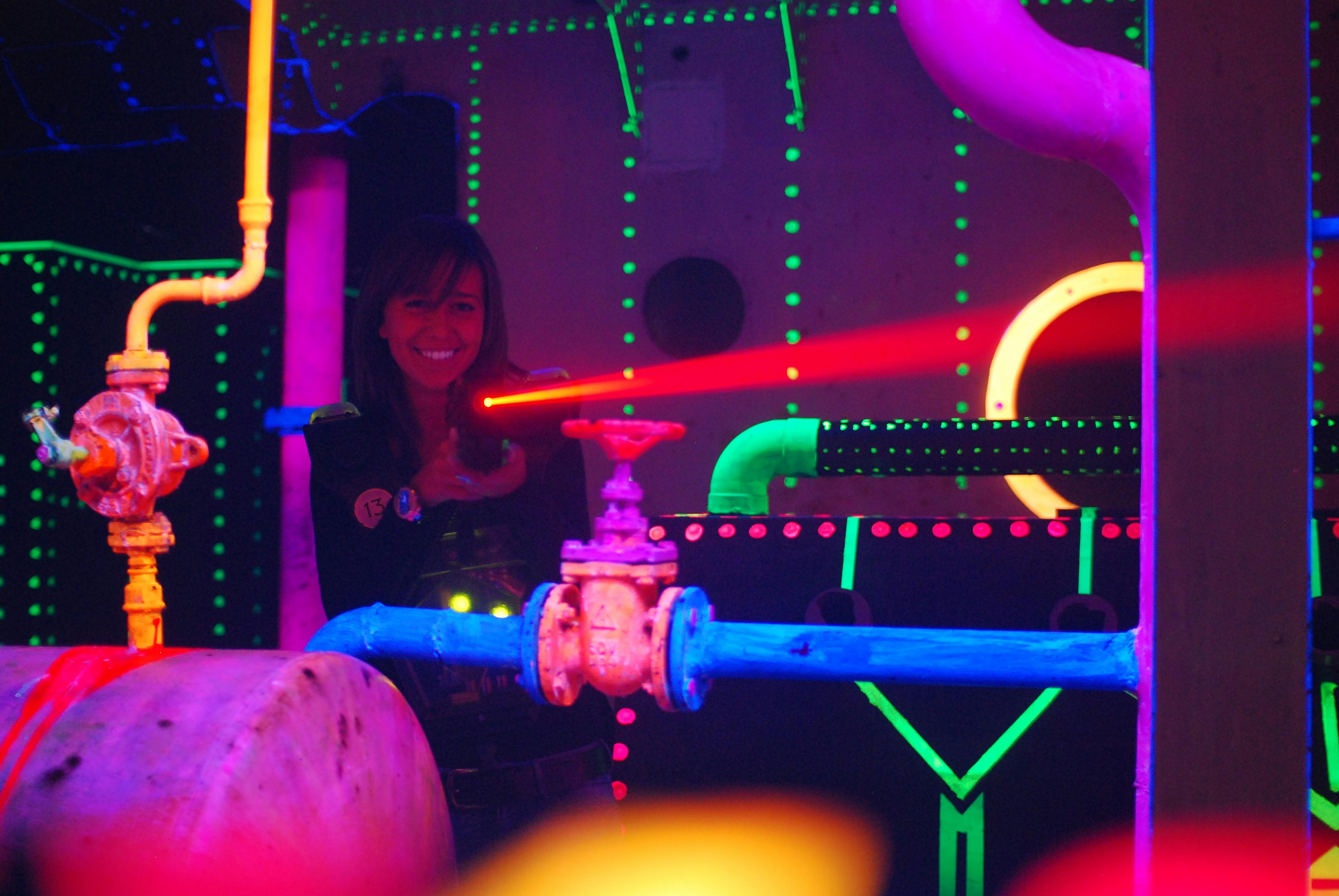 빛나는 파이프와 기계 구조가 있는 네온 조명 환경에서 빨간색 레이저 건을 조준하는 미소 짓는 사람.