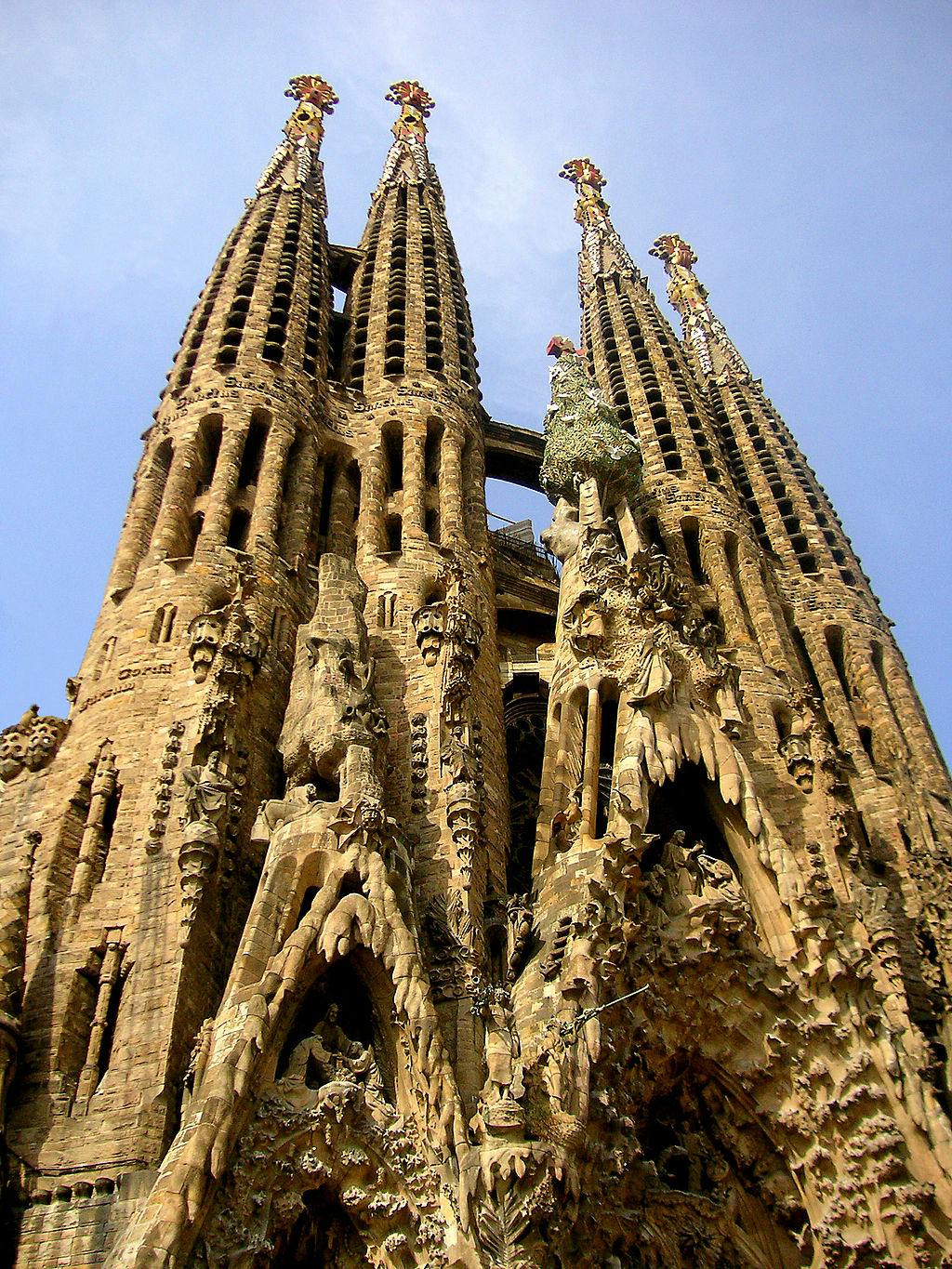 Ornate, towering stone spires of an elaborate Gothic-style cathedral reach towards a clear blue sky.
