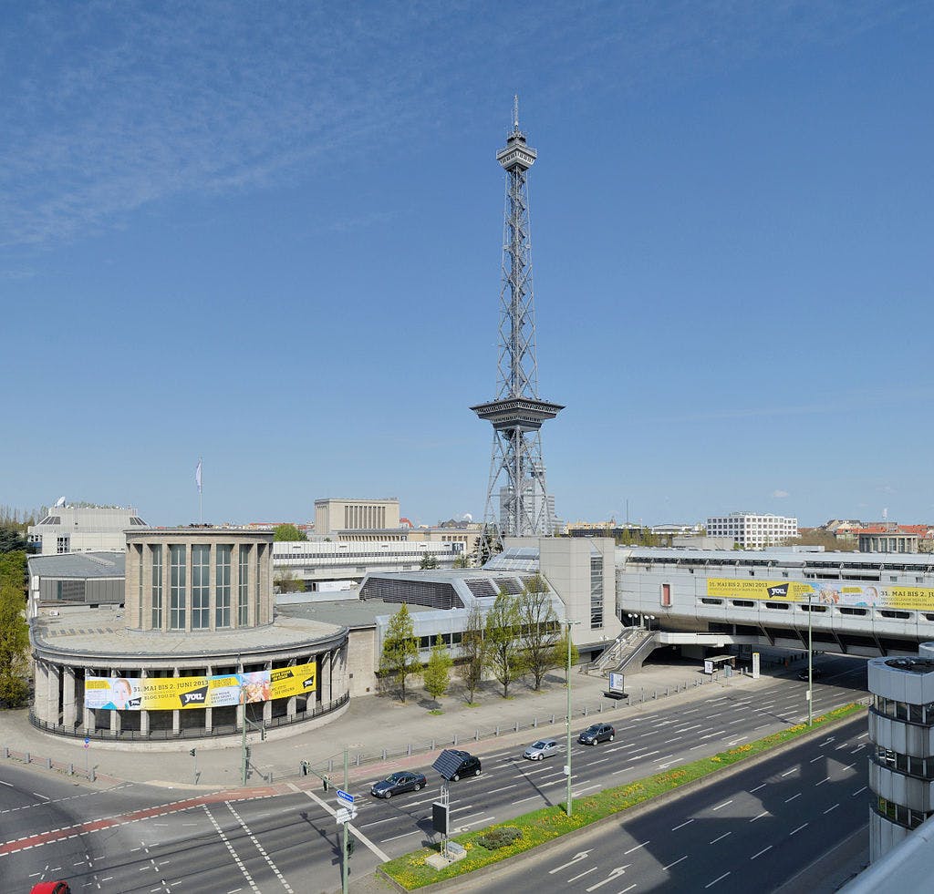 높고 격자 모양의 강철 타워, 여러 건물, 여러 대의 자동차가 있는 번화한 도로가 있는 도시 풍경.