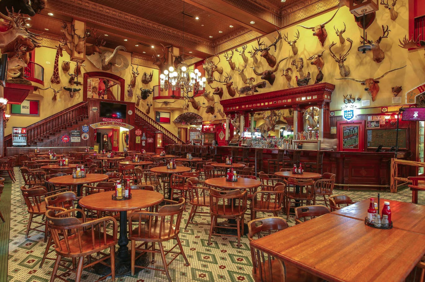 En rustik bar med træborde og -stole, dyreophæng på væggene, udsmykkede bardisker og vintage-skilte.