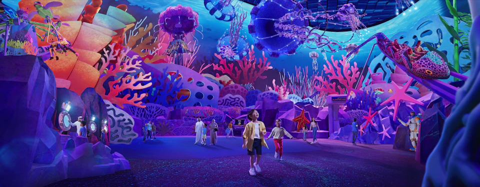 Children and adults exploring an underwater-themed exhibit with vibrant, colorful coral, jellyfish, and marine life decor.