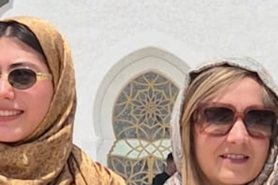 Three people in sunglasses pose in front of a white mosque with a domed roof and ornate architectural details.
