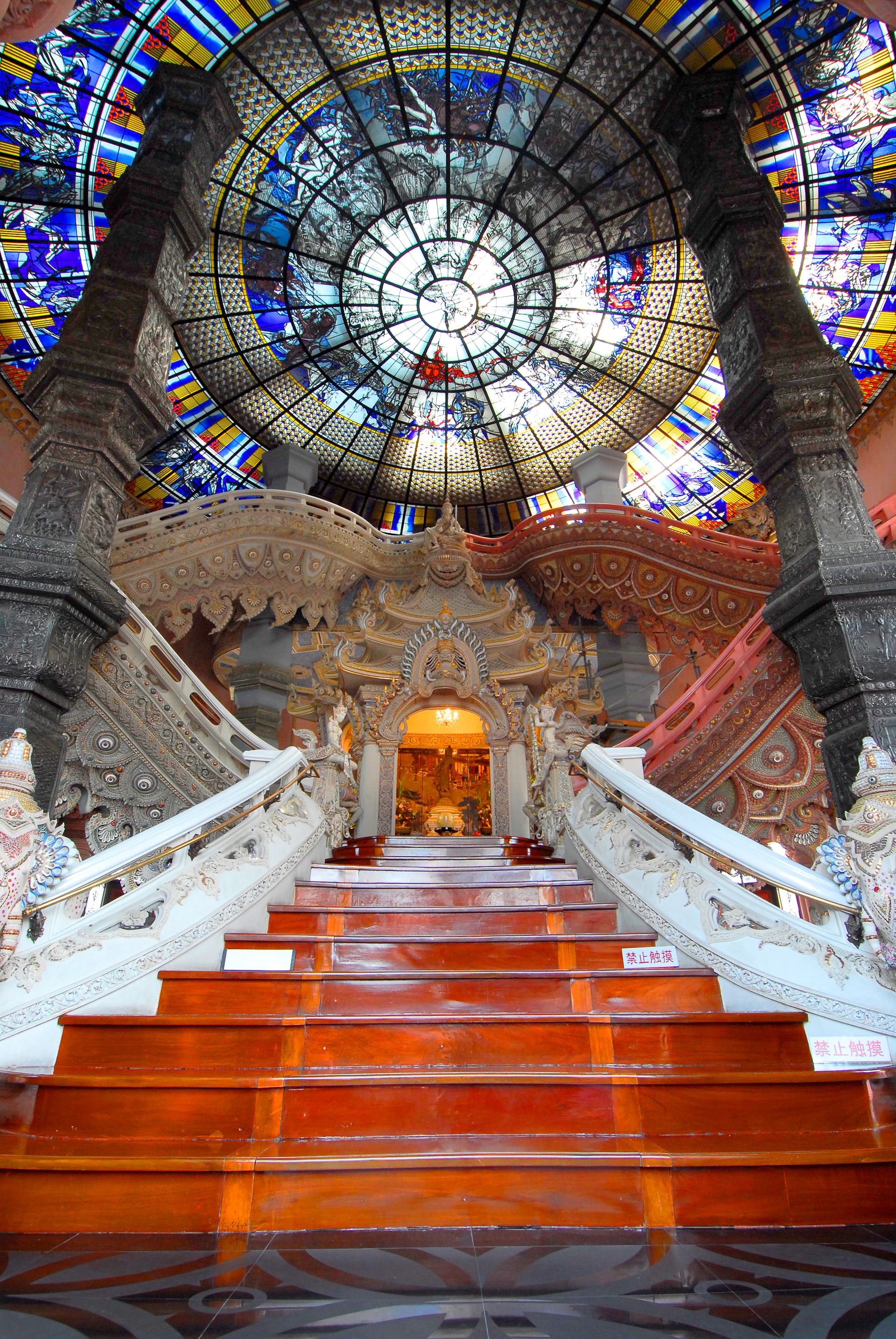Grand staircase in an elaborately decorated building with ornate carvings and a large stained-glass dome ceiling.
