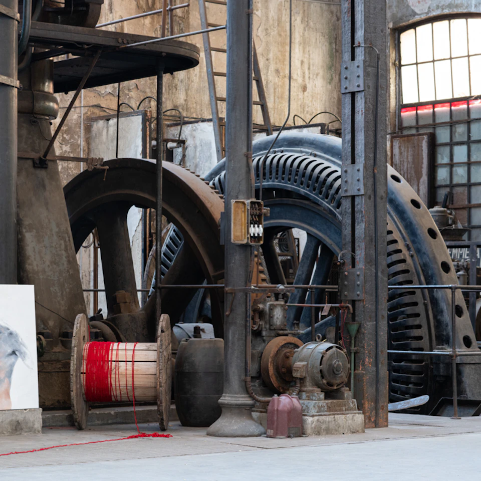 An old industrial workshop with large machinery, a spool of red wire, and a window in the background.