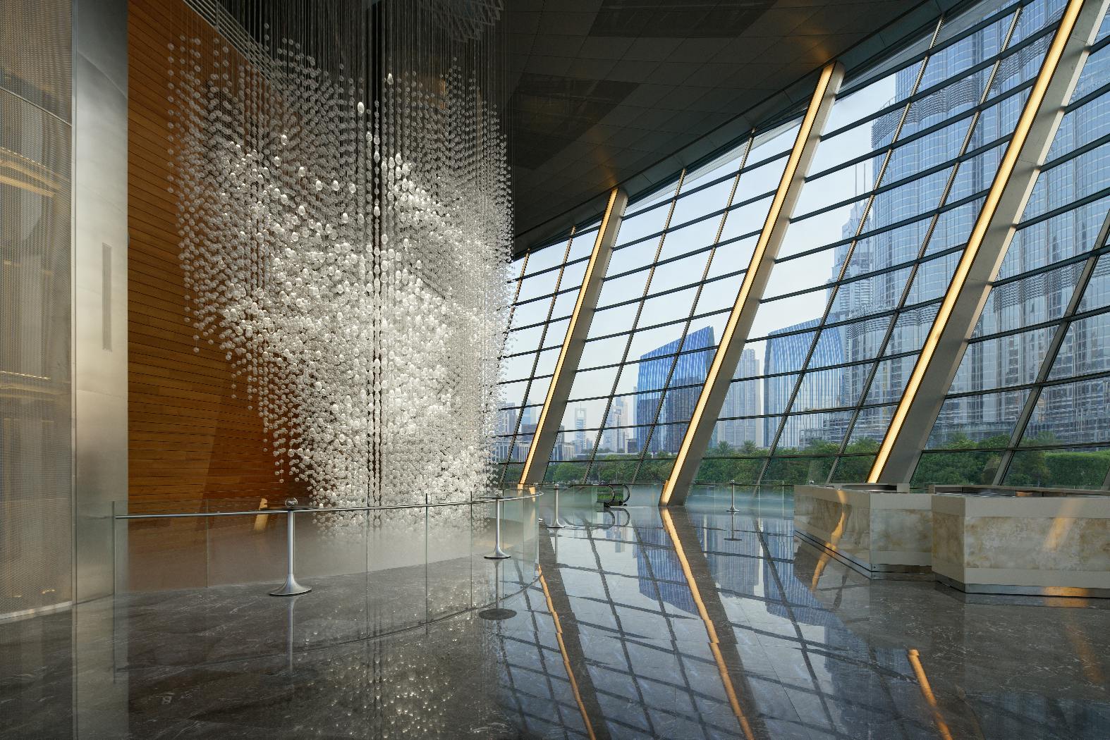 A modern, spacious atrium with a large, intricate hanging glass sculpture, floor-to-ceiling windows, and cityscape views outside.