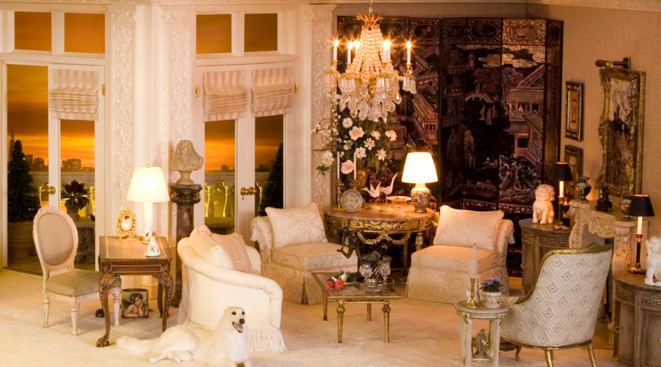 Elegant living room with cream-colored furniture, a chandelier, floral decorations, artwork, and a dog on the carpet.