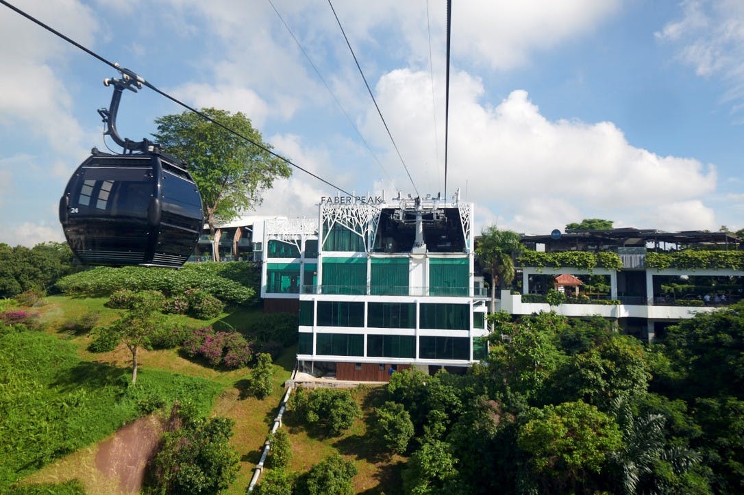 Téléphériques s&#39;approchant de la station de Faber Peak, entourés d&#39;une végétation luxuriante sous un ciel partiellement nuageux.