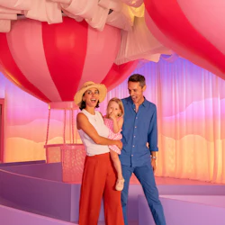 En leende familj står i ett färgglatt rum med stora rosa och röda luftballongdekorationer. På en skylt står det "Candy Studio".