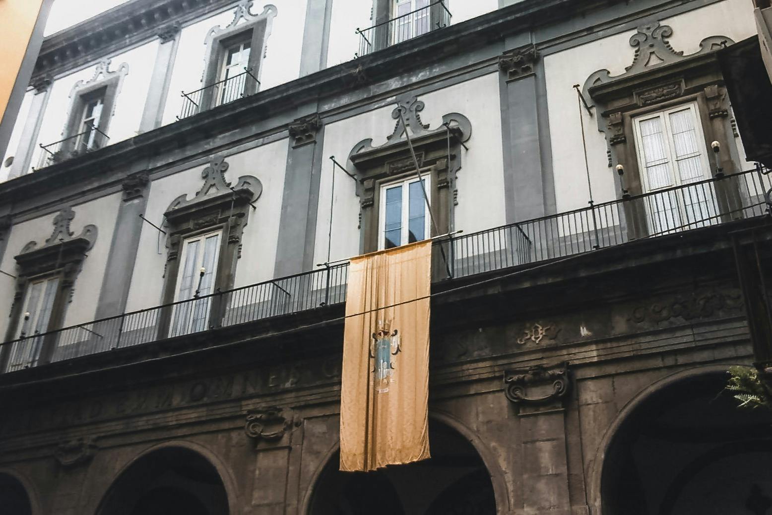 灰色和白色建筑，拱形门口，黄色横幅挂在阳台上。