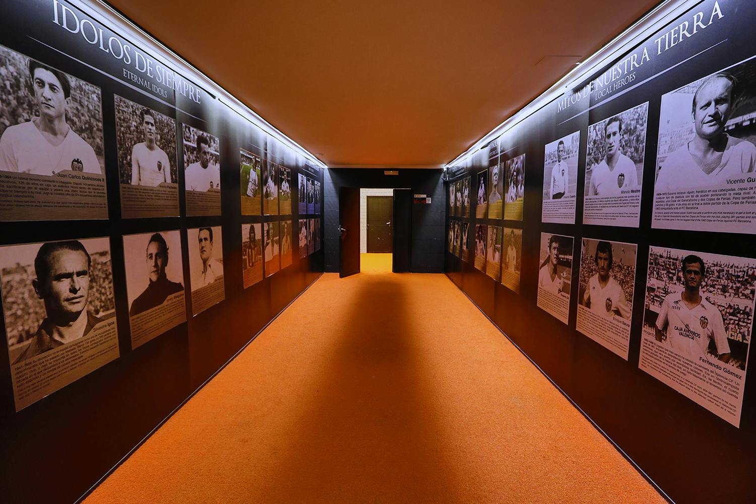 走廊上铺着橙色地毯，墙壁上摆满了有框肖像和著名体育人物的描述。 标志上写着“ÍDOLOS DE SIEMPRE”。