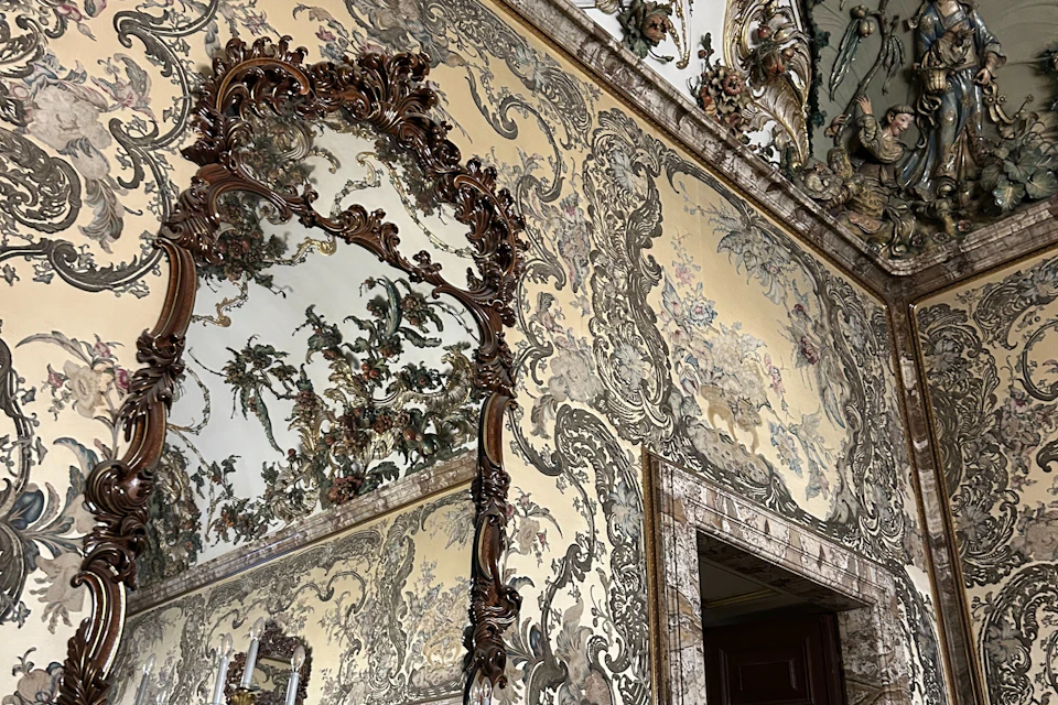 Ornate interior wall with intricate floral decorations and a large decorative mirror reflecting the room's decor.
