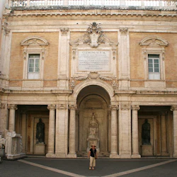 En person står på en innergård omgiven av klassisk arkitektur, statyer och skulpterade stenreliefer.