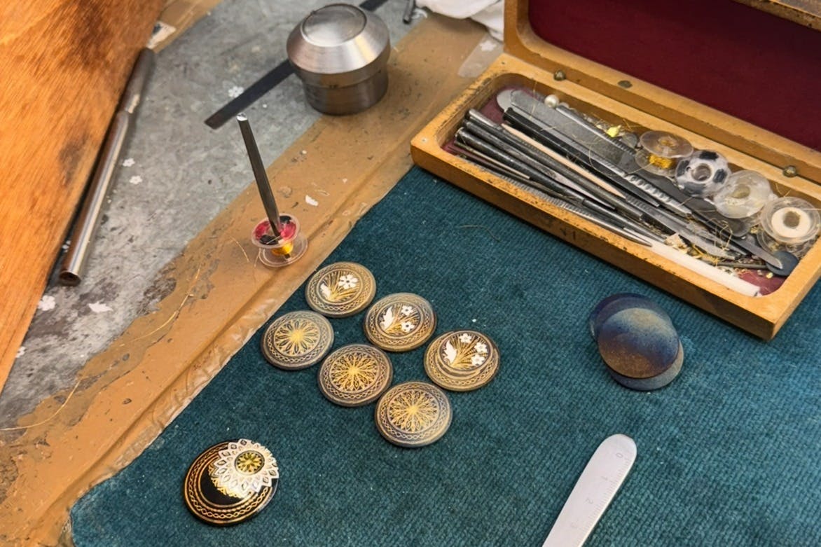 Un plateau de table avec des disques métalliques décoratifs, un ensemble d'outils dans une boîte, un petit support avec un disque et un tapis vert.