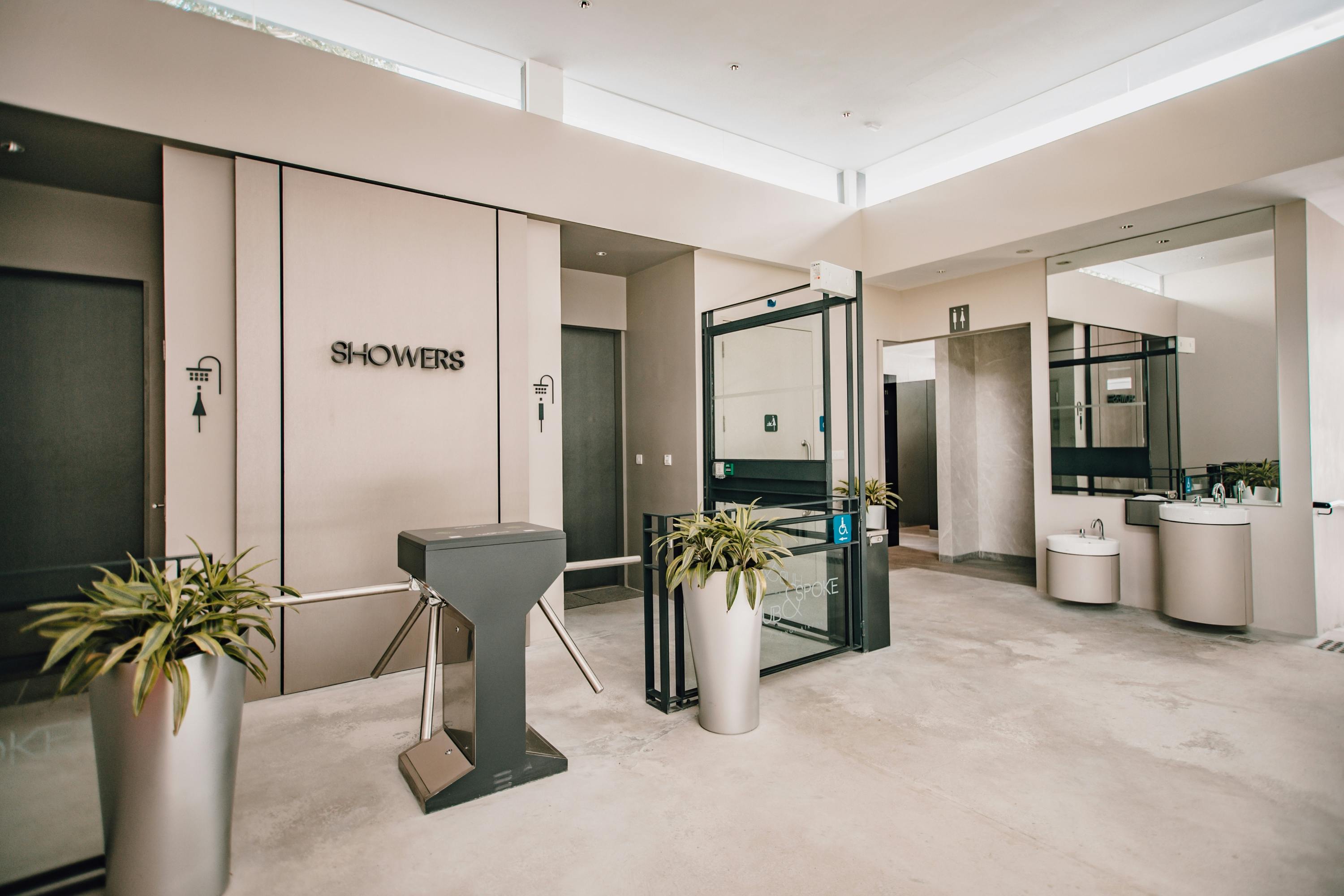 Modern indoor shower facility entrance with turnstile, potted plants, and accessible restroom signs.