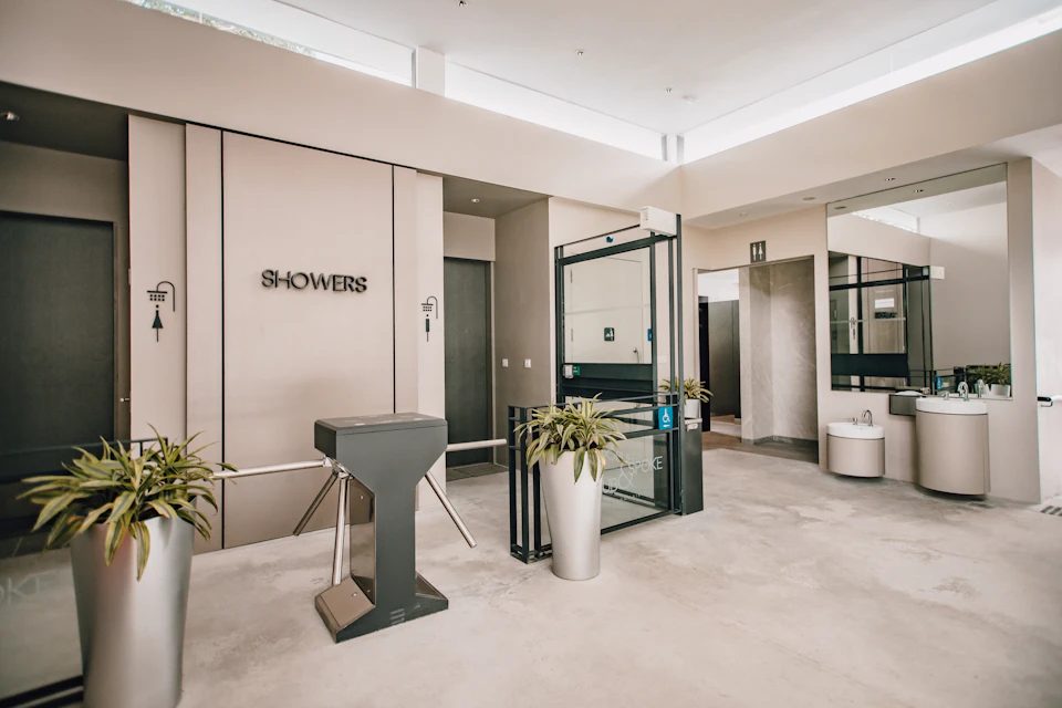 Modern indoor shower facility entrance with turnstile, potted plants, and accessible restroom signs.