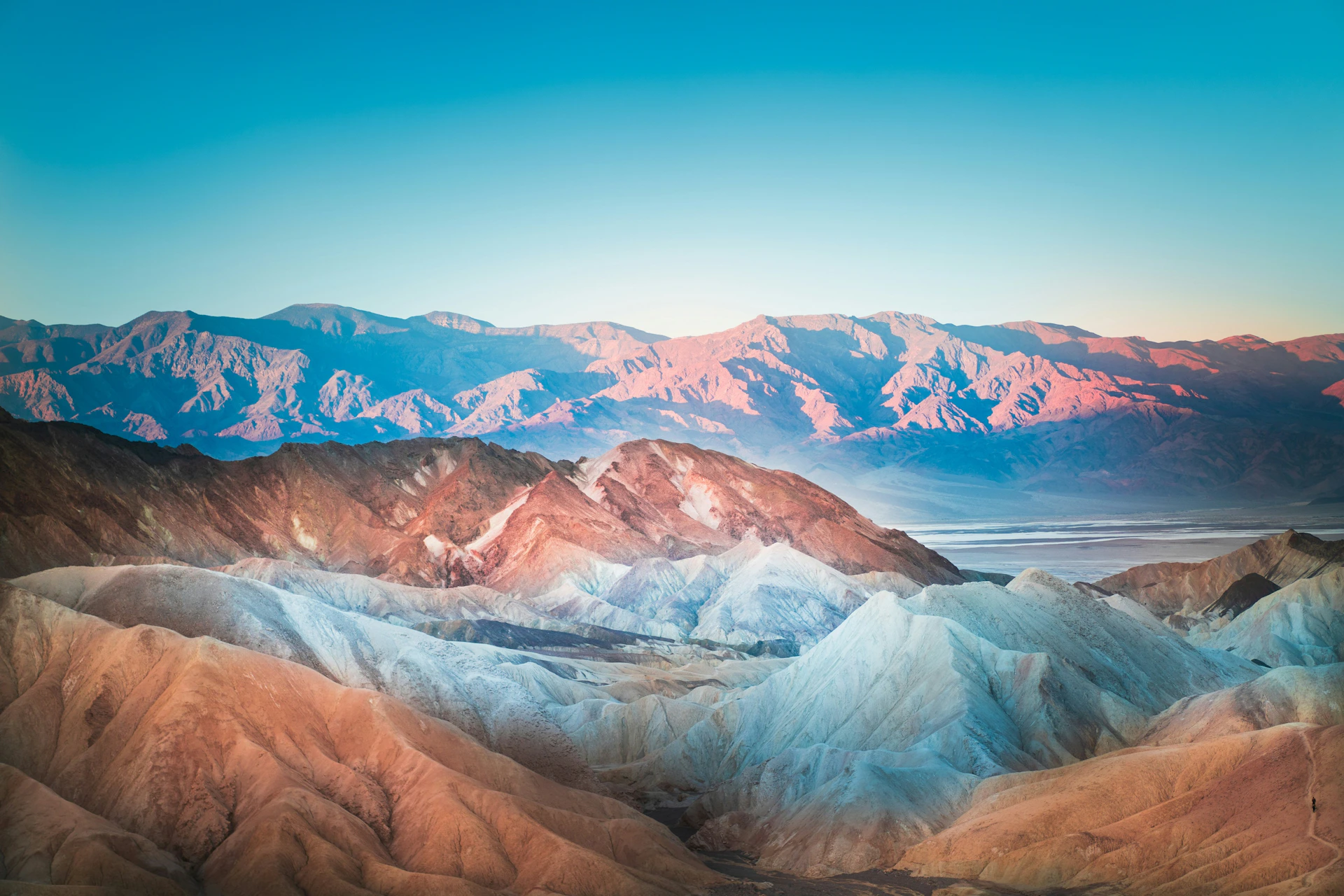 A scenic view of colorful mountain ridges under a clear sky, with layers of terrain in varying hues and textures.