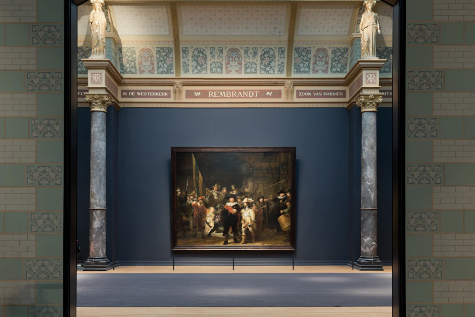 A museum gallery displaying a large painting by Rembrandt, framed by ornate architecture with columns and decorative details.