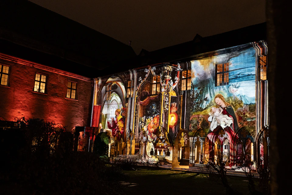 A building facade at night illuminated with colorful projected art featuring religious motifs and figures.