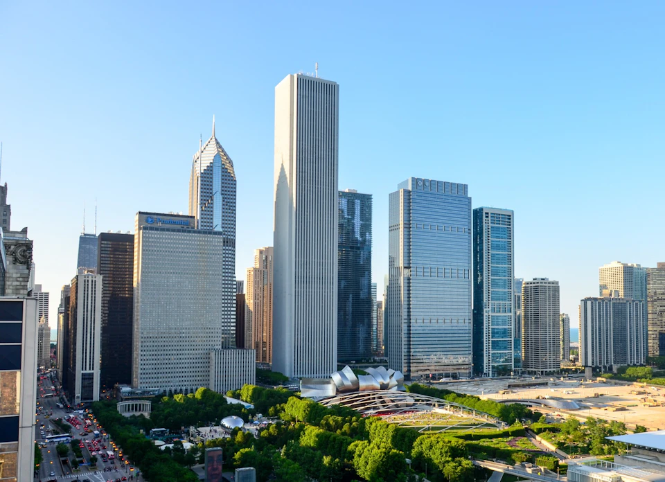 Skyline of tall buildings and skyscrapers with a park in the foreground, under a clear blue sky.