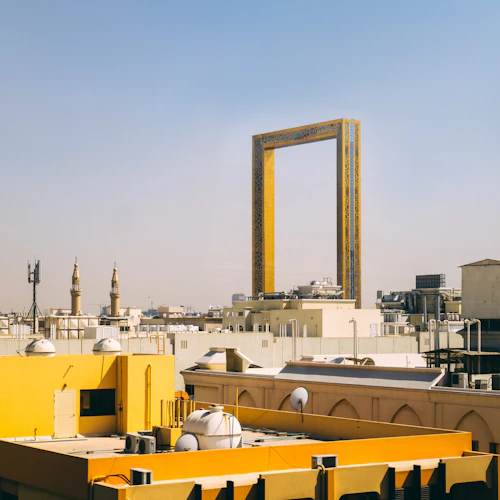Urban skyline with yellow buildings and the prominent rectangular Dubai Frame in the background against a clear sky.