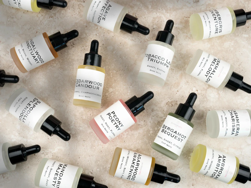 Assorted dropper bottles with labeled essential oils, arranged on a light marble surface, featuring different scents.
