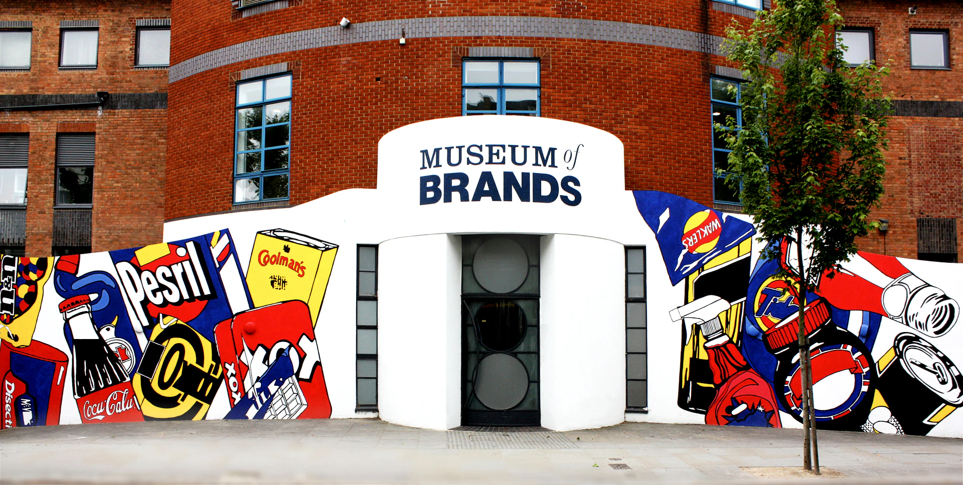 Brick building facade with "Museum of Brands" signage above entrance, surrounded by colorful graphics of branded products.