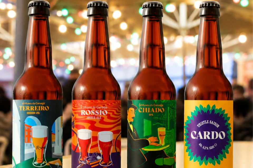 Four craft beer bottles with colorful labels, set against a blurred background with festive lights.