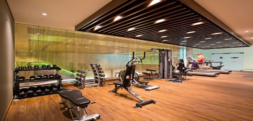 A modern gym with various exercise equipment, including weight racks, machines, and benches, on a wooden floor.