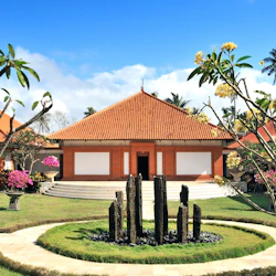 A building with a red-tiled roof and white walls, surrounded by manicured gardens and flowering trees.